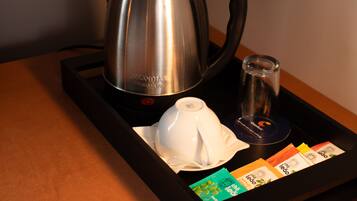 Una tetera de acero inoxidable, una tetera blanca, un vaso y bolsitas de té sobre una bandeja.