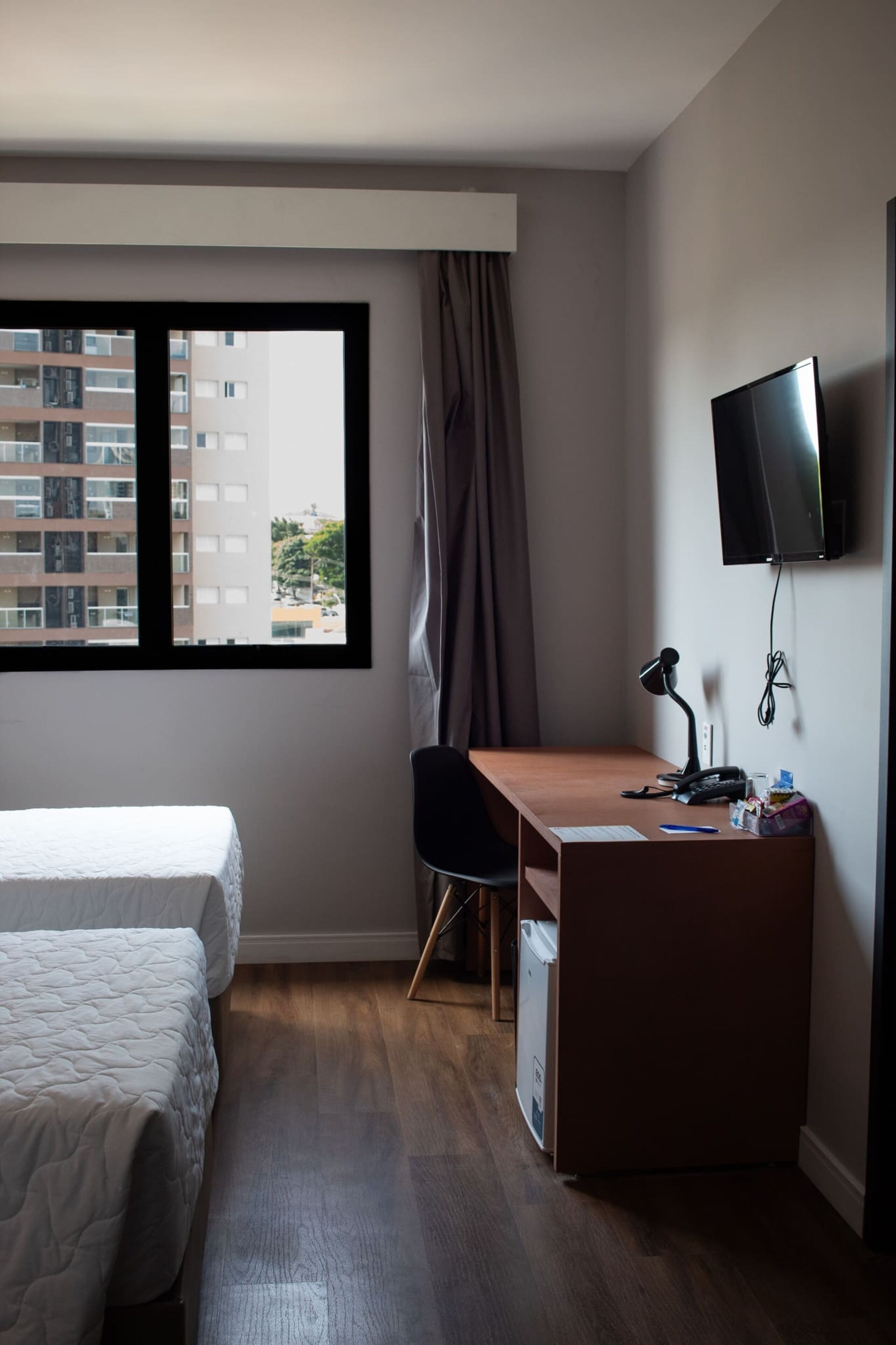 A hotel room with two beds, a desk with a chair, a television, and a window with curtains.