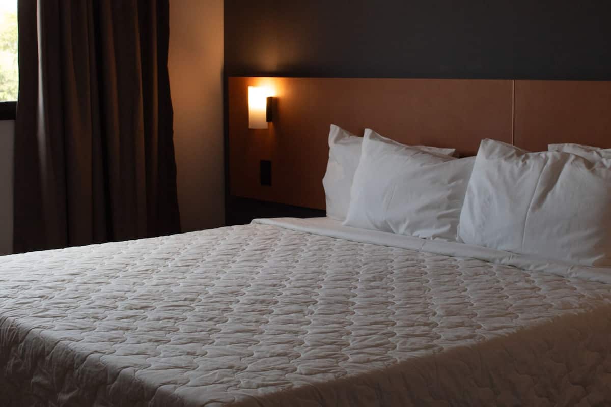 Une chambre d’hôtel avec un grand lit, une tête de lit dotée d’une lampe et une fenêtre avec des rideaux.