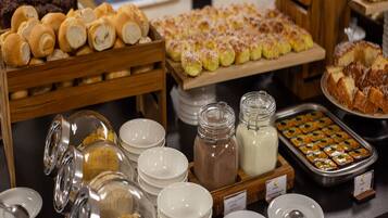 Buffet com diversos alimentos, incluindo pastelaria, pão e sobremesas.