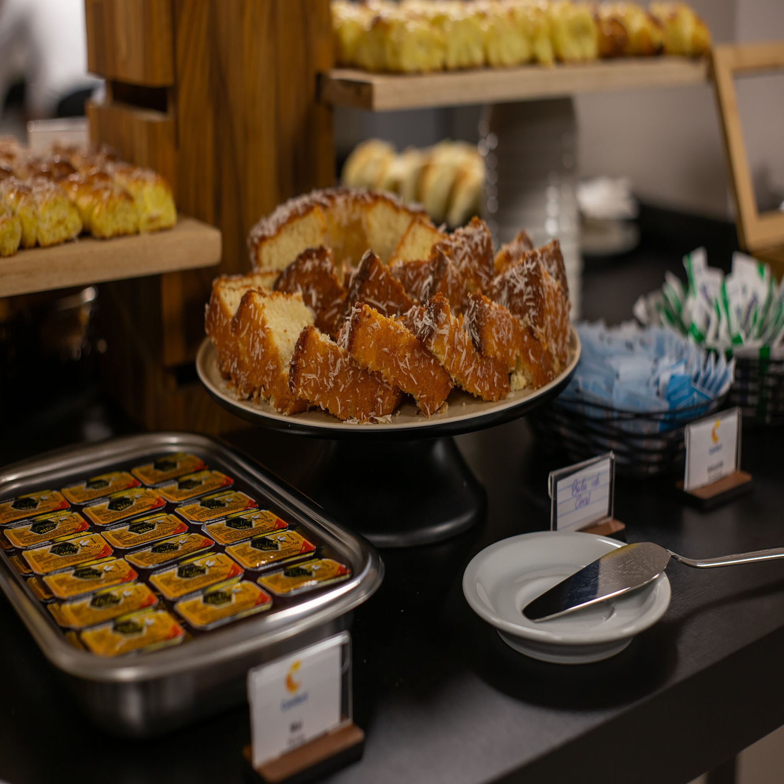 A buffet with various desserts, including a cake with coconut flakes, a tray of assorted pastries, and a dish with a spoon.