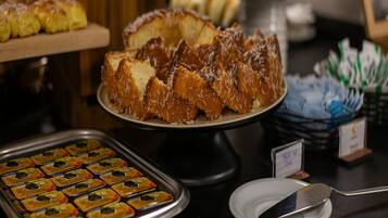 A buffet with various desserts, including a cake with coconut flakes, a tray of assorted pastries, and a dish with a spoon.