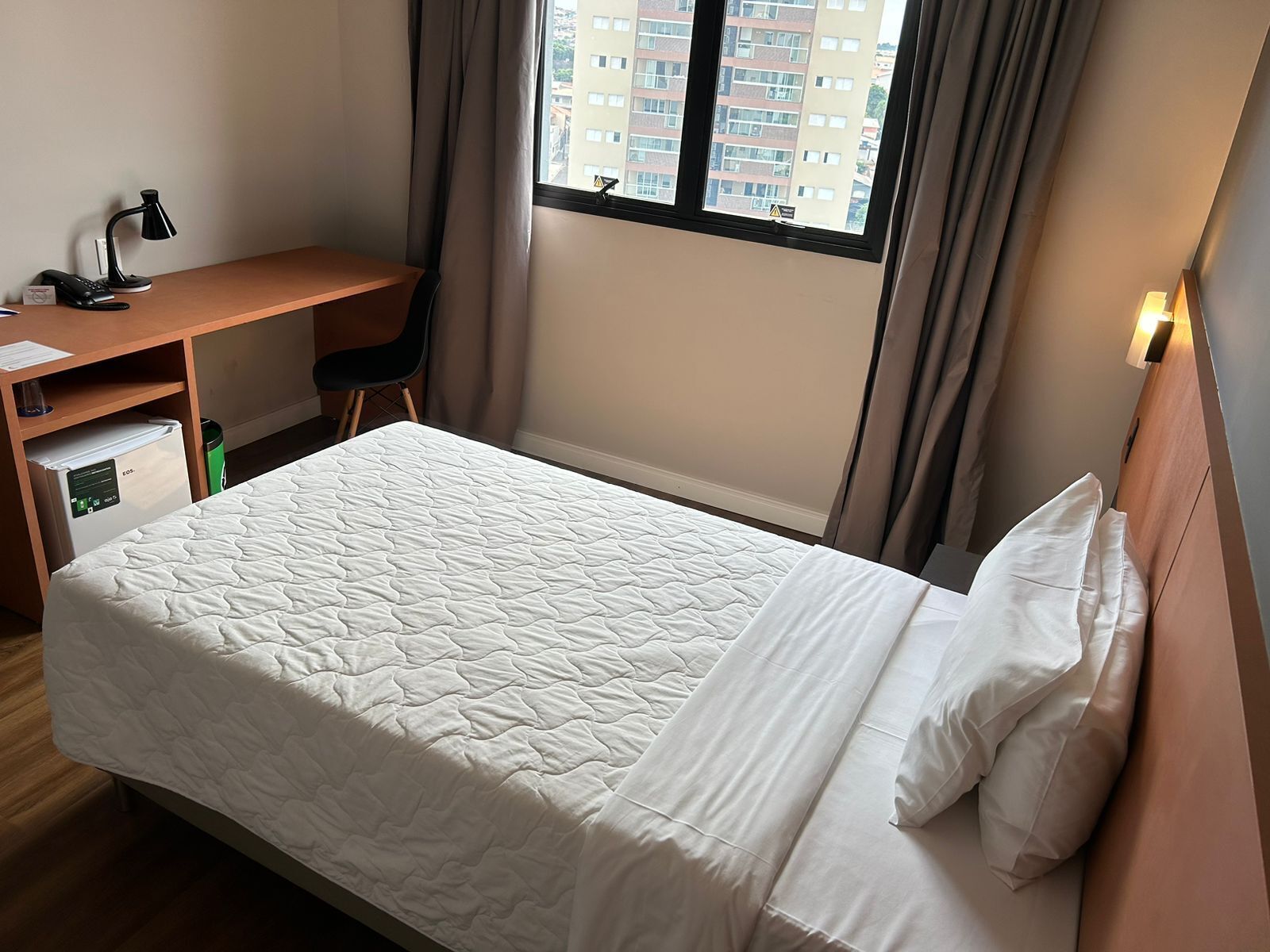 Une chambre d’hôtel avec un lit, un bureau, une chaise et une fenêtre avec des rideaux.
