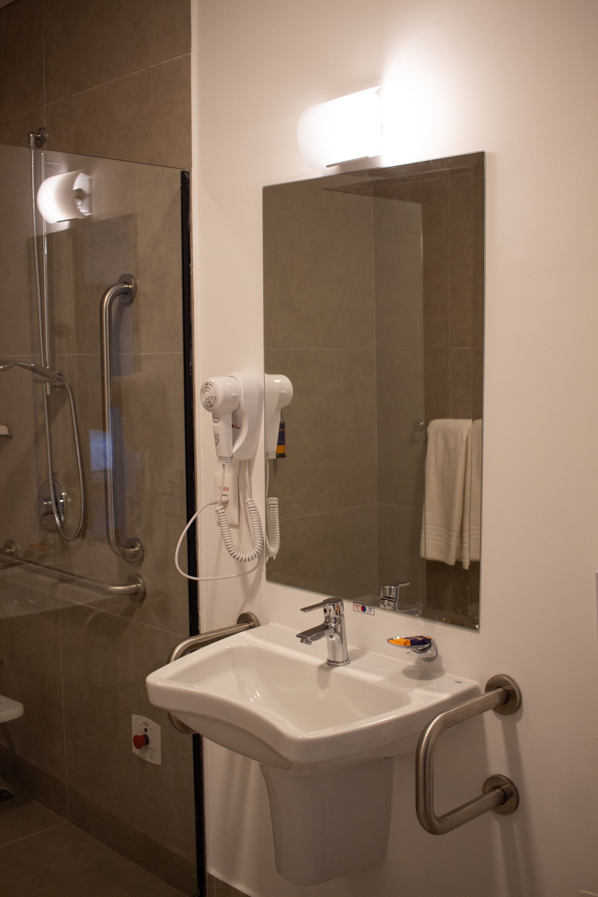 A bathroom with a glass shower enclosure, a white sink with a hand dryer, and a mirror above the sink.