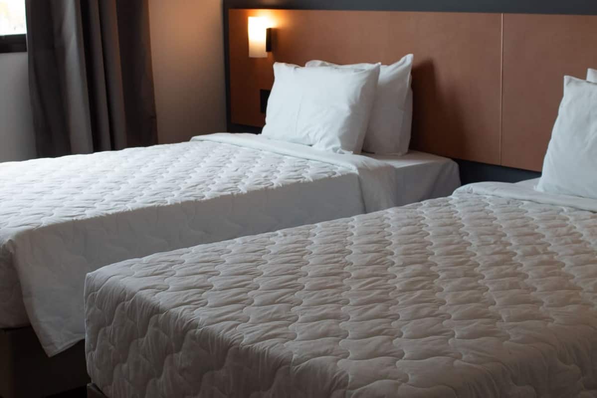 Deux lits avec du linge de lit blanc dans une chambre d’hôtel.