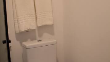 A bathroom with a toilet, a towel rack with two towels, a toilet paper holder, and a shower hose.
