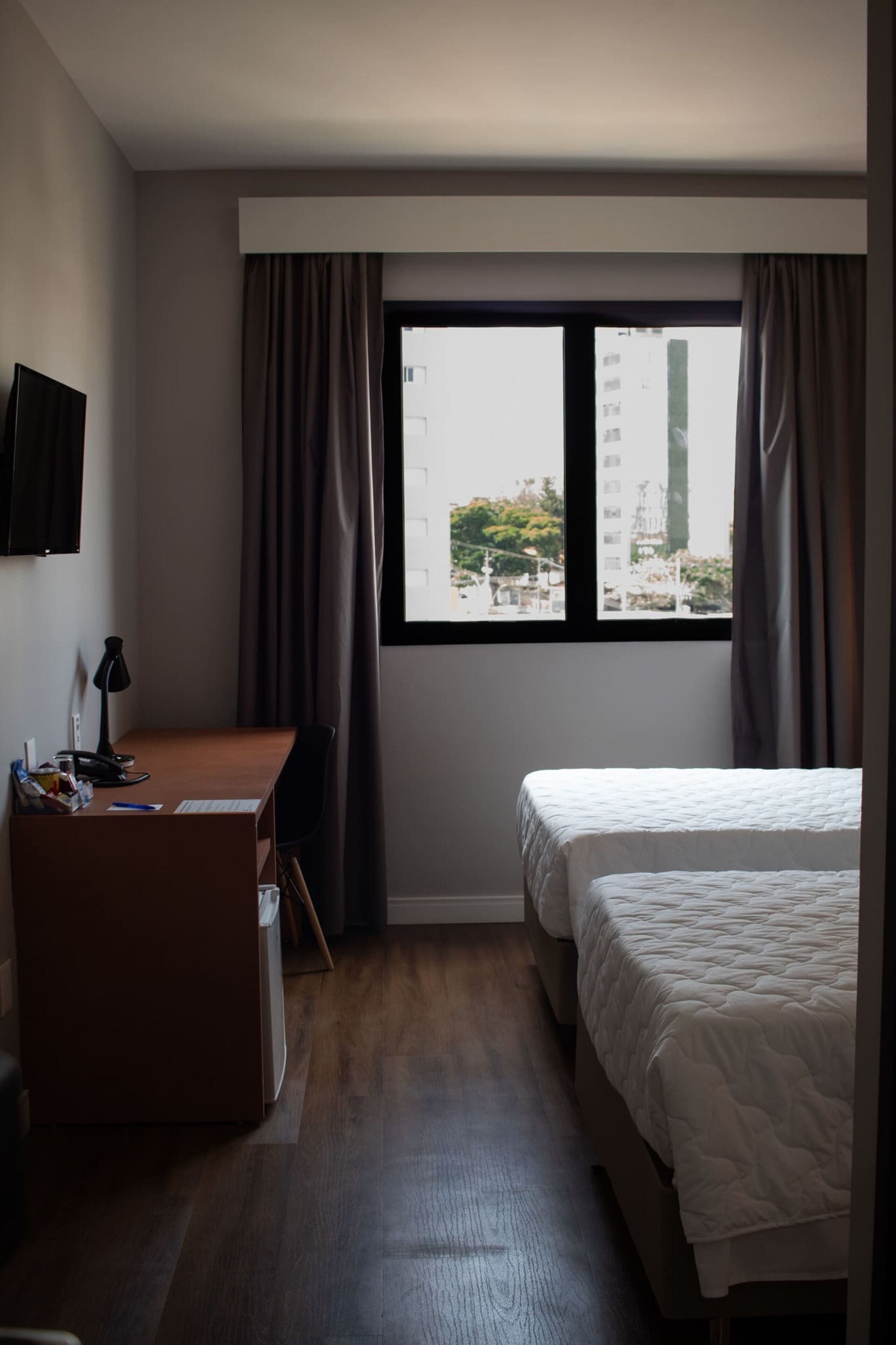 A hotel room with a bed, a desk, a chair, and a window with curtains.