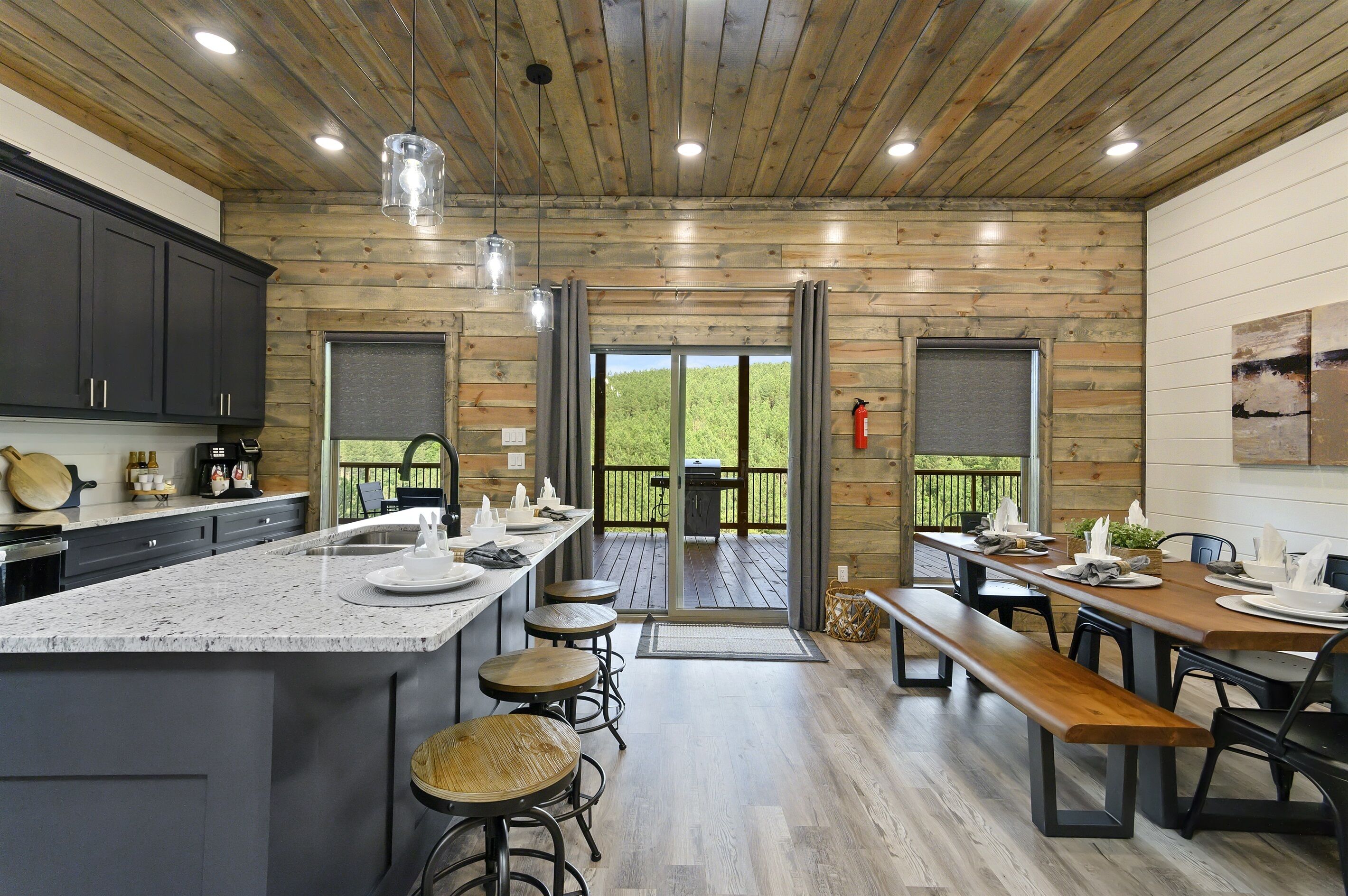 A modern kitchen with granite countertops, wooden cabinets, and a large island with stools. There are two dining areas with wooden tables and benches.