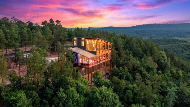 A multi-story wooden cabin surrounded by dense forest, with a clear view of the landscape. - Hilltop Retreat | 3BR Cabin with Mountain Views, Hot Tub & Game Rm | Sleeps 14 (Broken Bow)