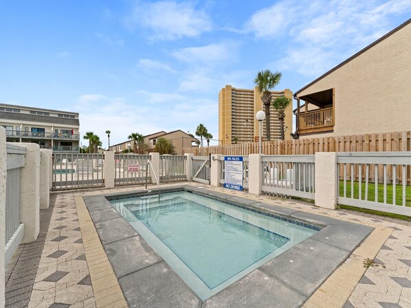 Piscina com deck ladrilhado, cercada por grade e deck de madeira.