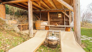 A rustic wooden cabin with a stone wall, a wooden bench, and a table with wine glasses. - Vineyard Cottages Rataj (Novo Mesto)