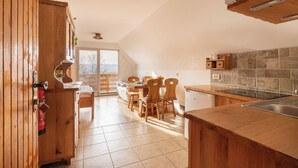 A kitchen with wooden cabinets, a dining area with a table and chairs, and a view of the outdoors. - Vineyard Cottages Rataj (Novo Mesto)