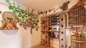 A rustic interior with a stone floor, wooden shelves with wine bottles, and a wall-mounted tree with grapevines. - Vineyard Cottages Rataj (Novo Mesto)