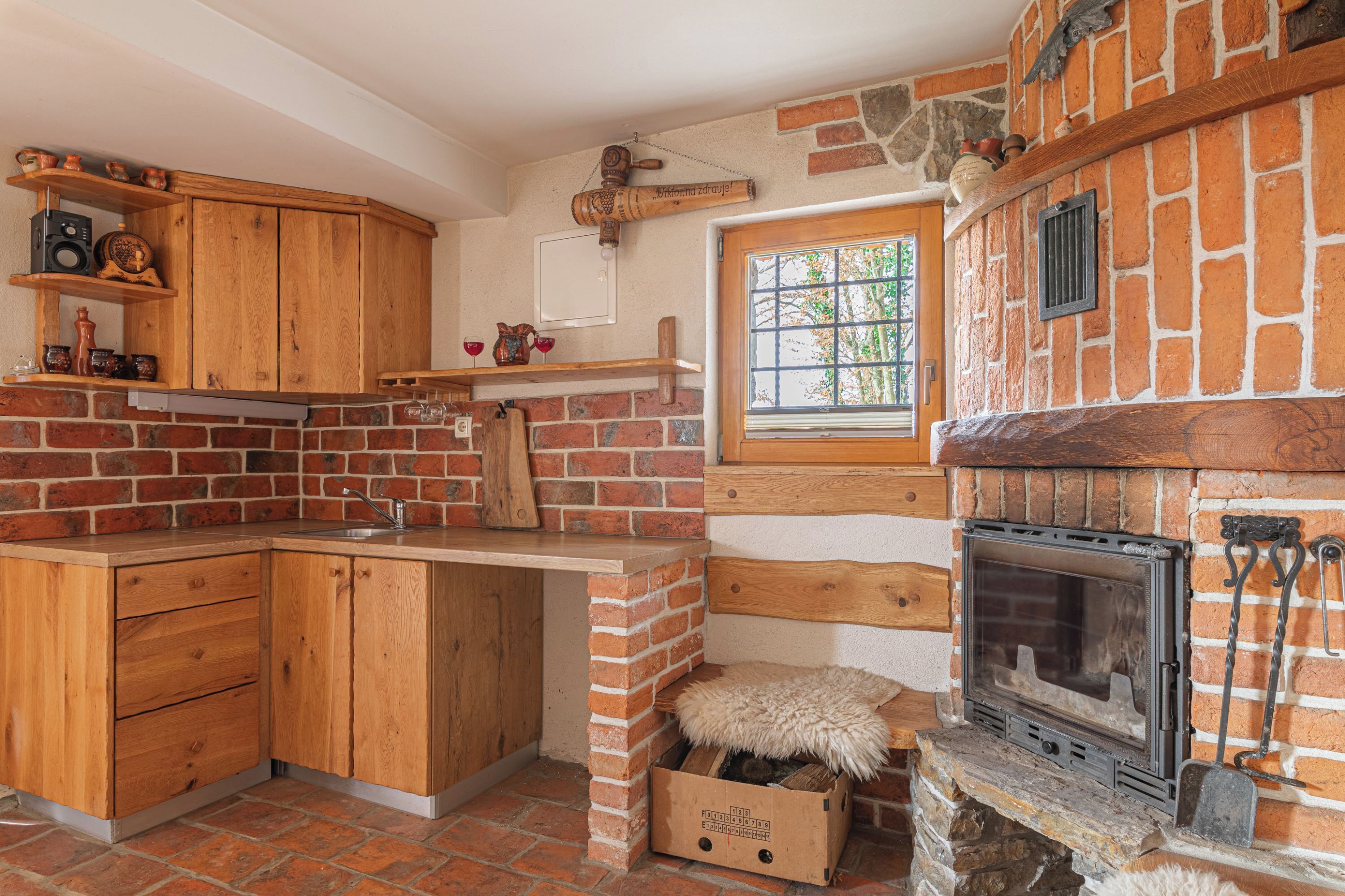 Une cuisine rustique avec des meubles en bois, une cheminée en briques et une fenêtre donnant sur un paysage verdoyant.