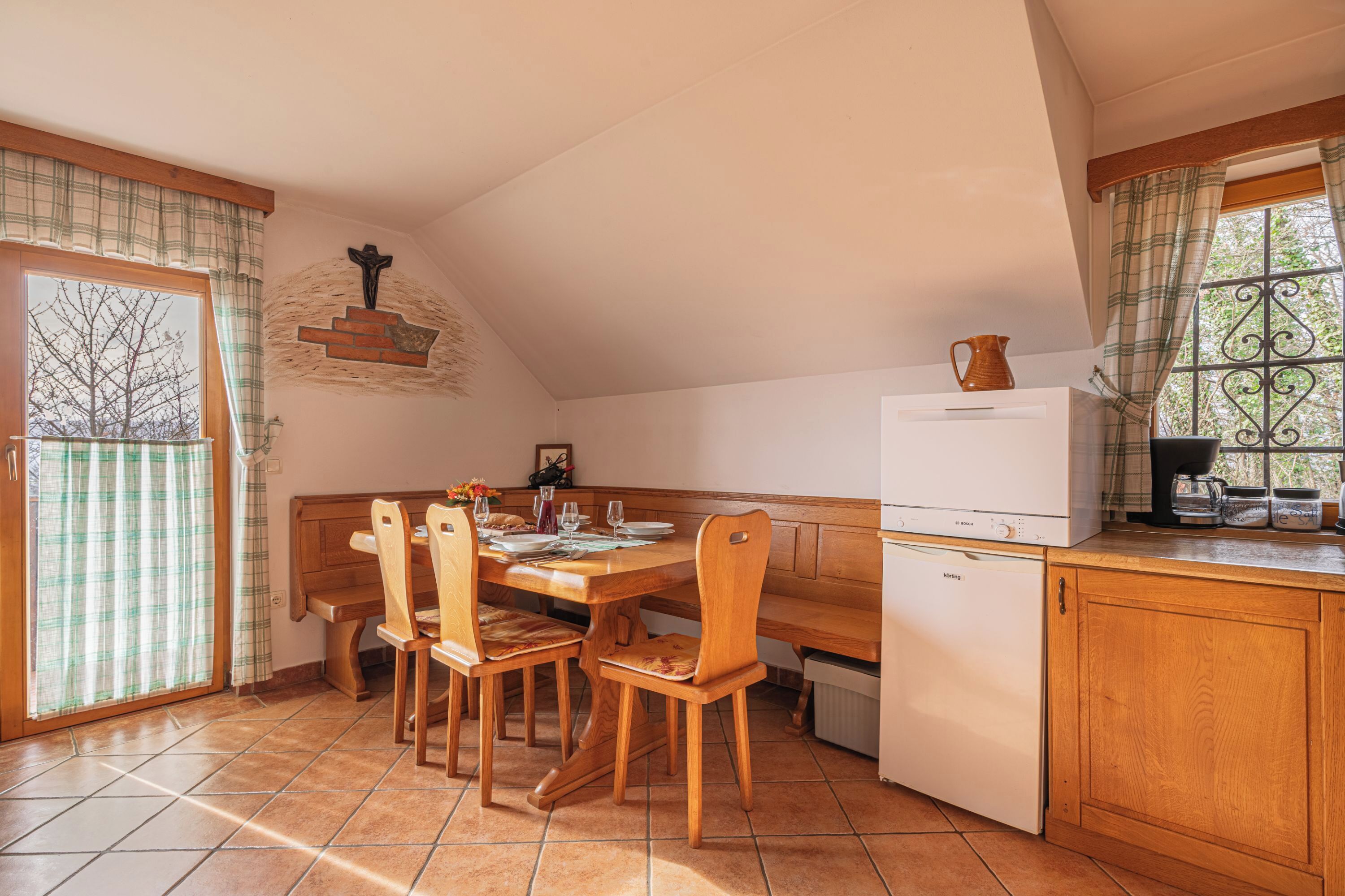 Een gezellige keuken met een houten tafel en stoelen, een witte koelkast en een raam met gordijnen.