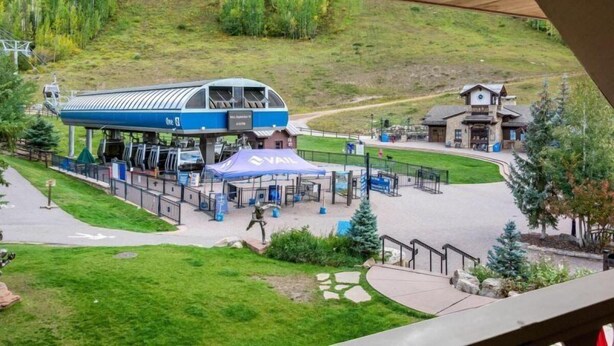 Estância de esqui com uma estação de teleférico azul e branca, uma área de espera coberta e um chalé ao fundo.