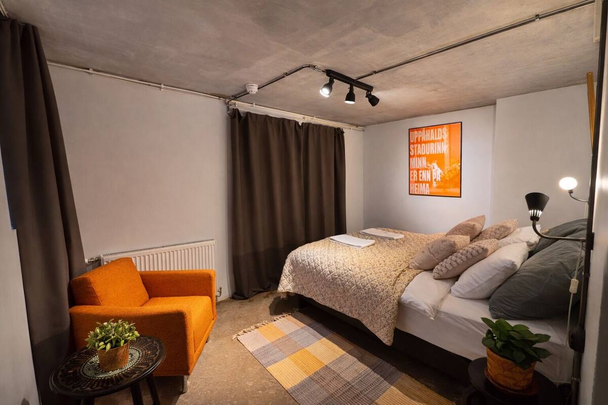Une chambre à coucher moderne avec un lit, un canapé, une petite table avec une plante et une affiche accrochée au mur.