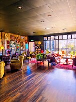 A spacious room with wooden flooring, a large window, and various pieces of furniture including chairs, a sofa, and a table.