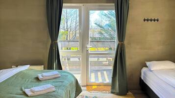 A hotel room with two beds, a green bedspread, a floral rug, a ceiling-mounted light fixture, and a view of a balcony with a railing.