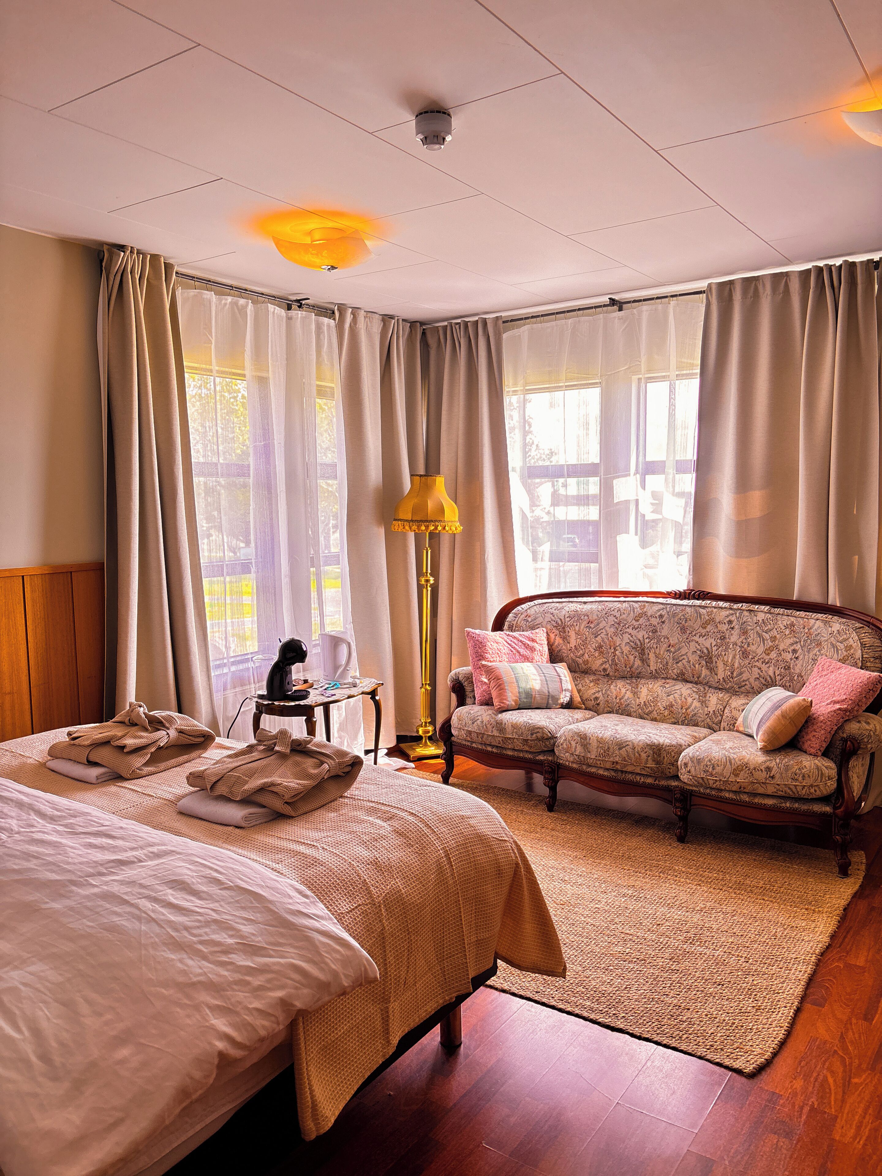 A hotel room with two beds, a sofa, a lamp, and a view of the outdoors.