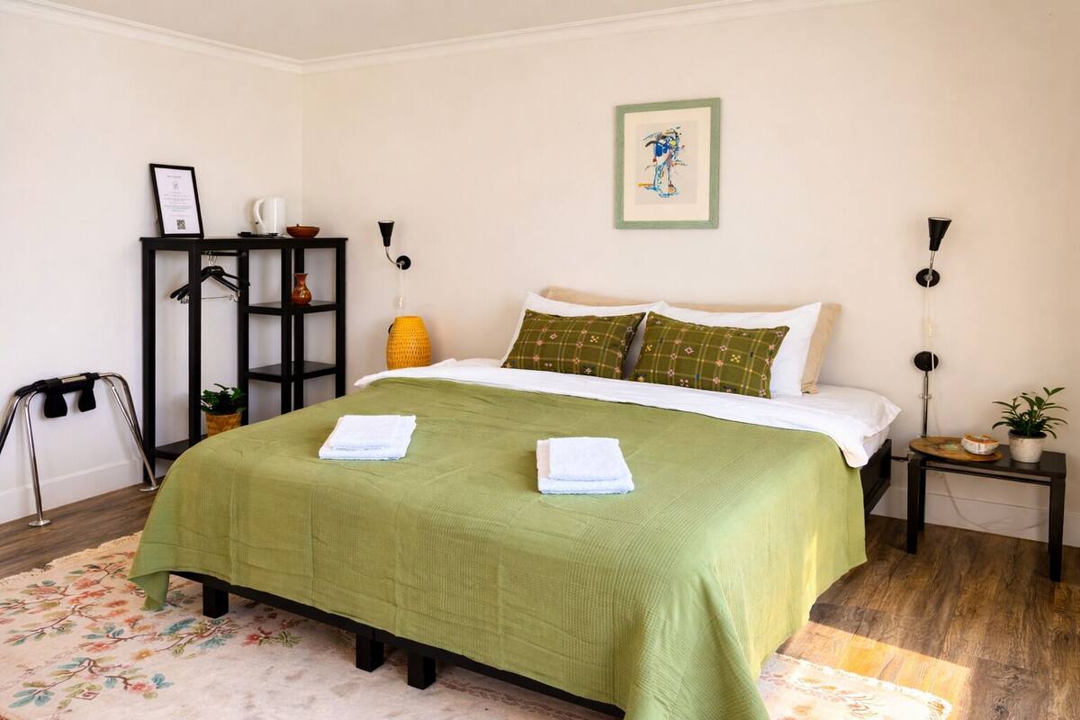 Une chambre bien rangée, avec un lit, une table de chevet, une étagère fixée au mur et un tableau encadré accroché au mur.