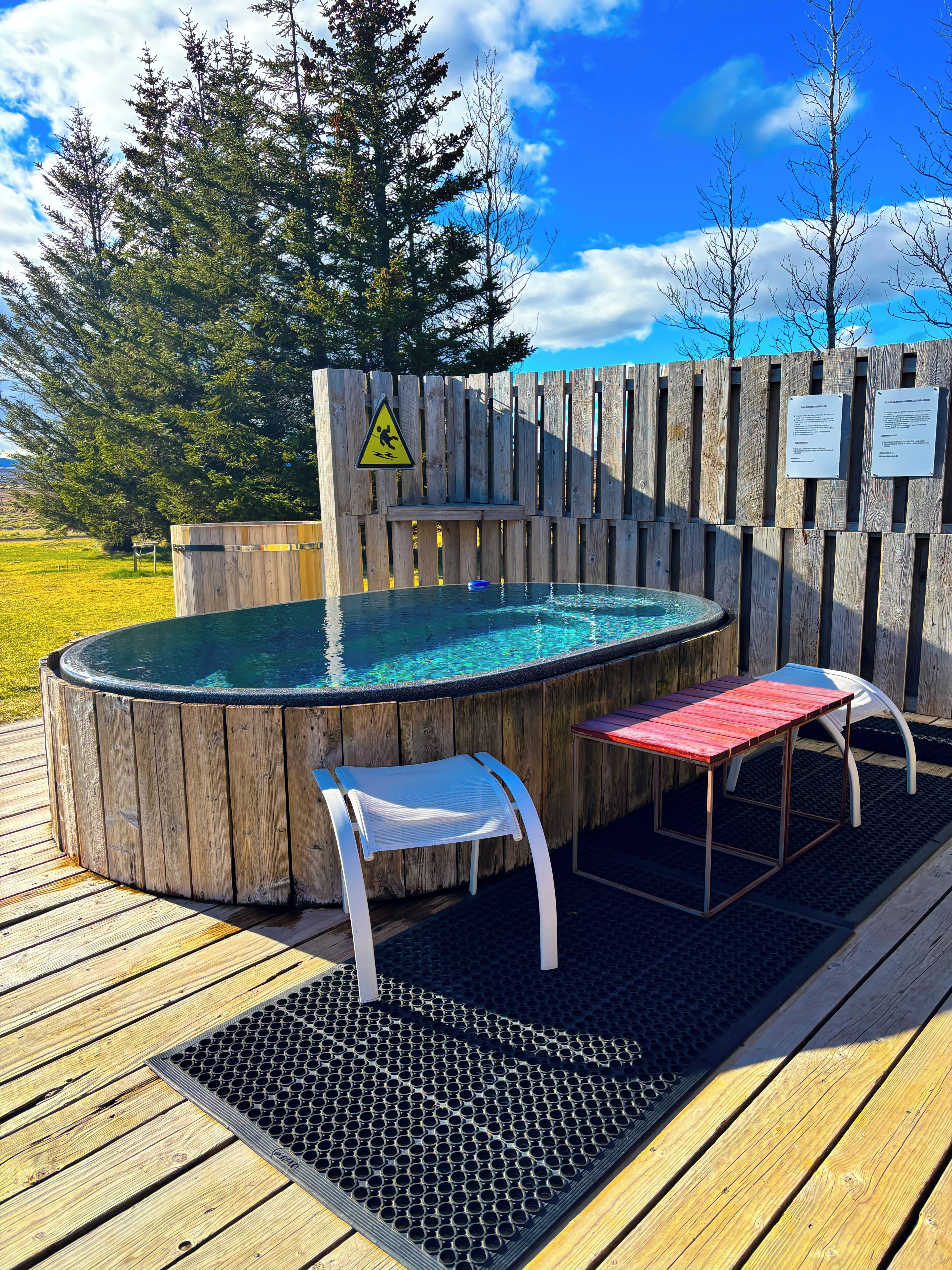 A hot tub with wooden walls, a wooden deck, and a chair.