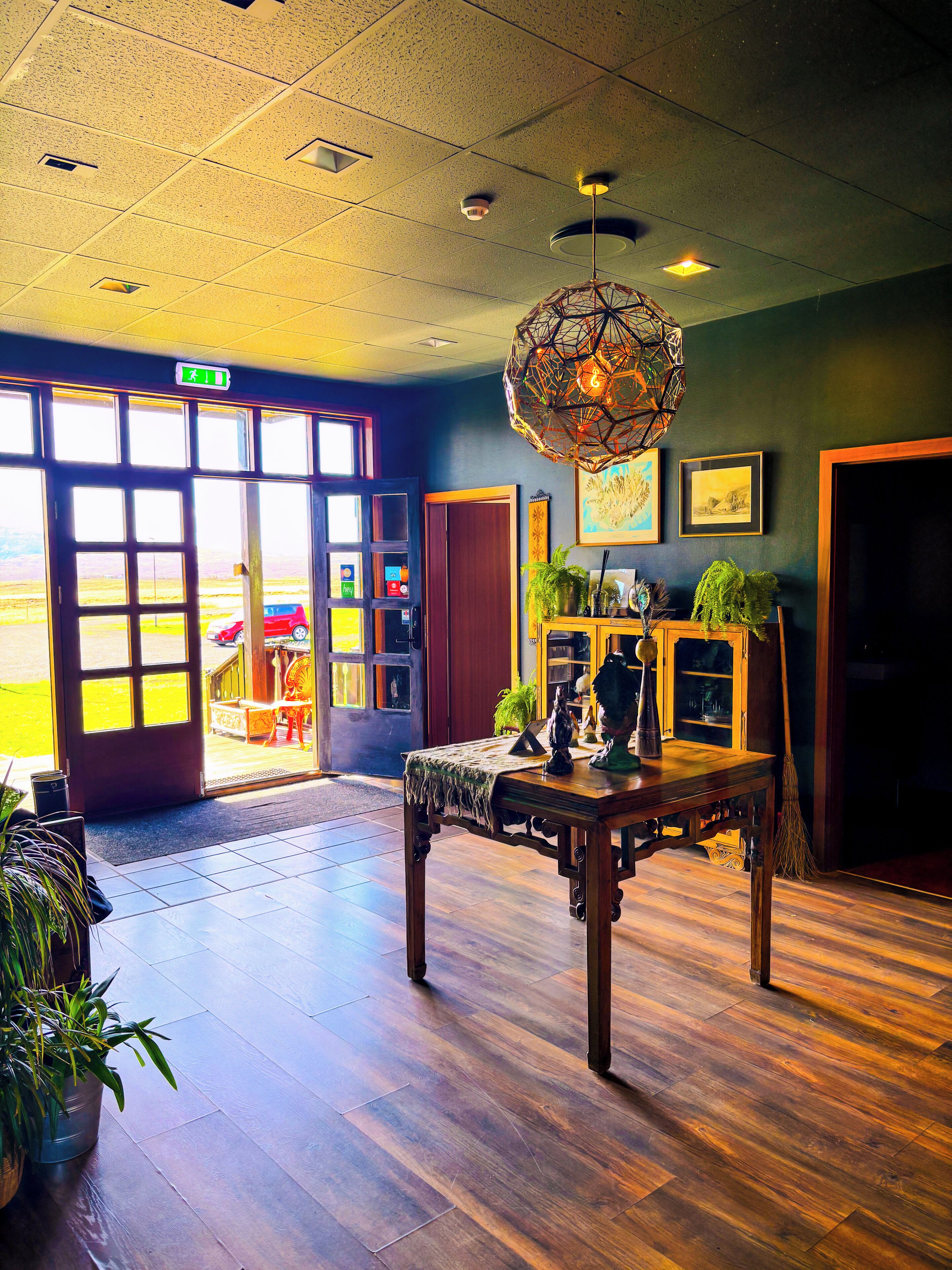 A spacious lobby with a wooden floor, a large table with decorative items, and a view of the outside through large windows.