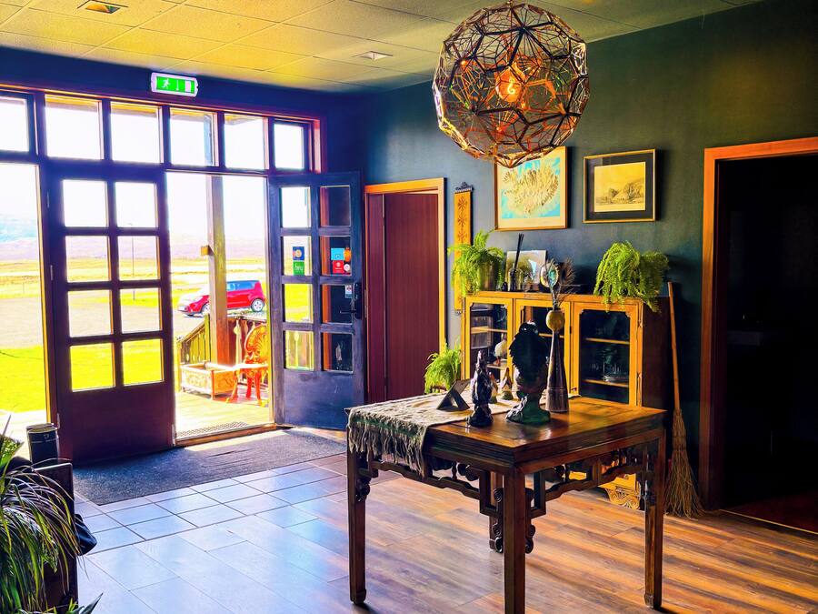 A spacious lobby with a wooden floor, a large table with decorative items, and a view of the outside through large windows.