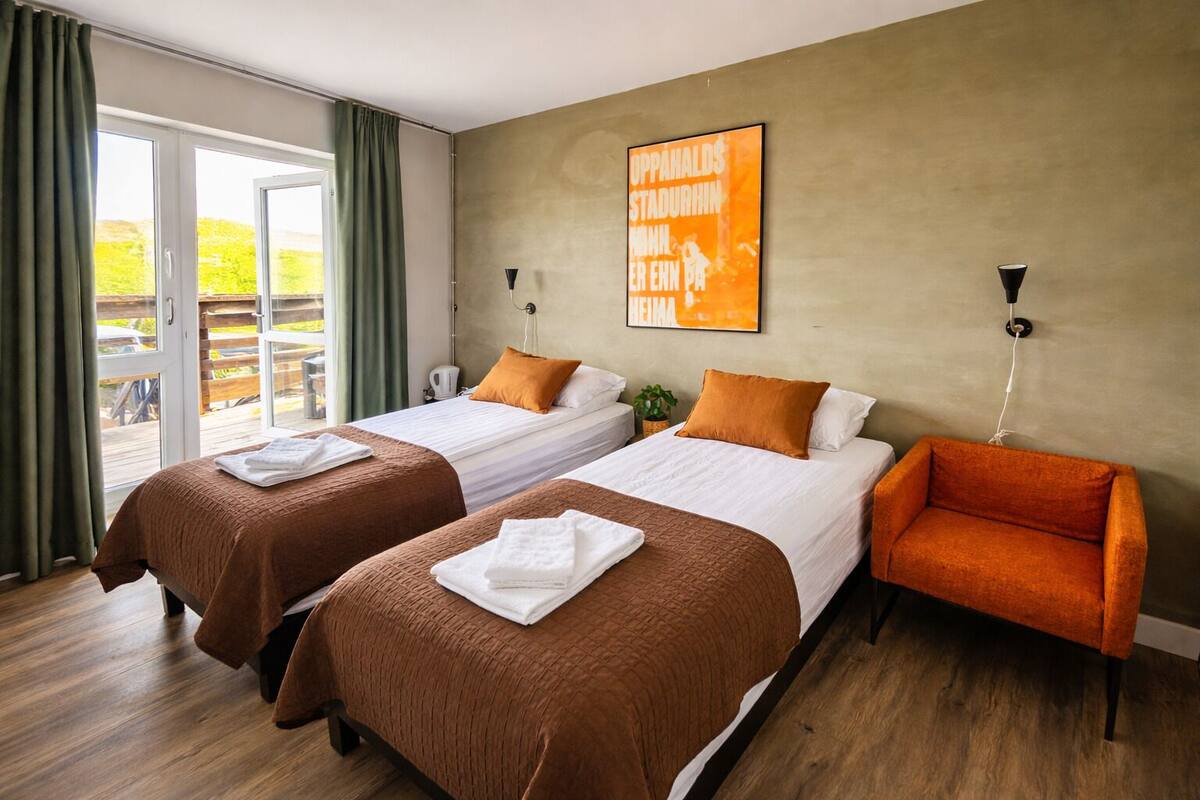 Une chambre d’hôtel avec deux lits, un canapé, une grande fenêtre avec des rideaux et une œuvre d’art accrochée au mur.