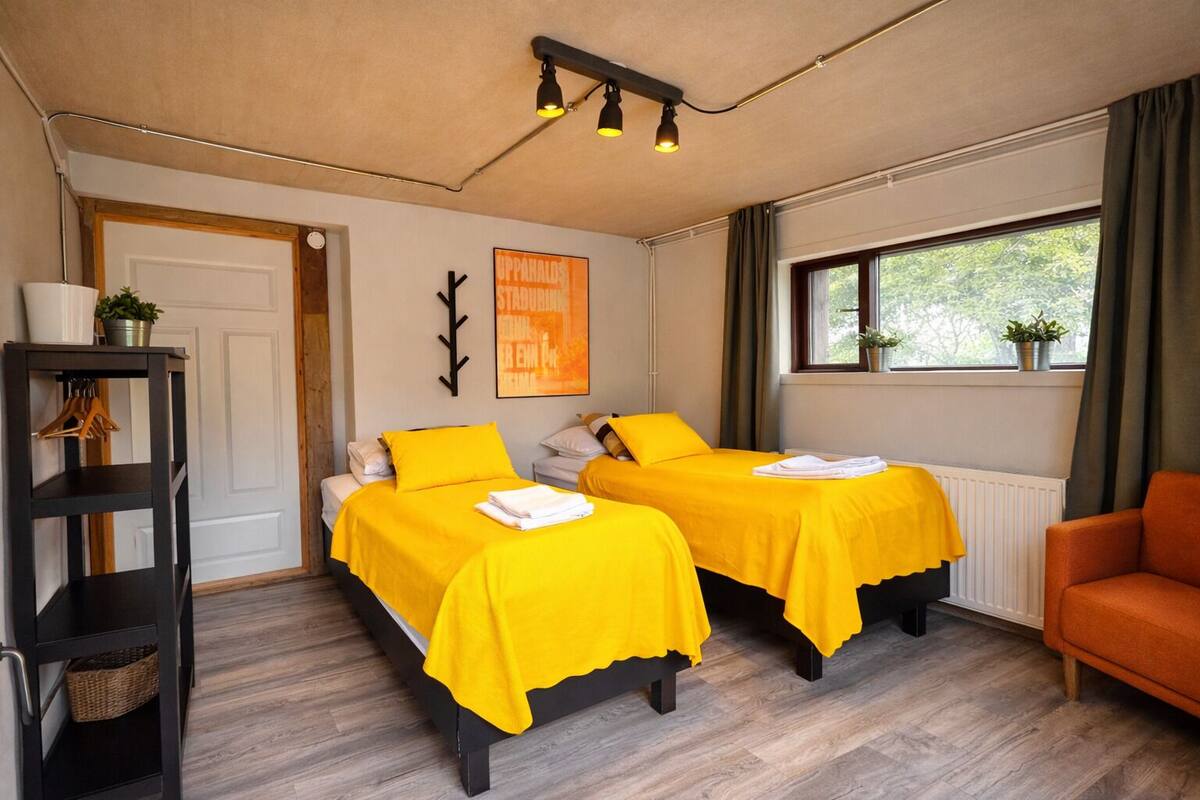 Une chambre avec deux lits, une chaise, une étagère, un radiateur et une fenêtre avec des plantes.