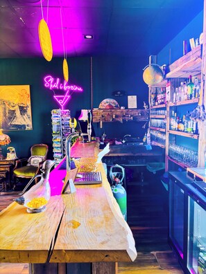A bar area with wooden tables, hanging lights, and shelves of bottles. - Hotel Brú countryside (Selfoss)
