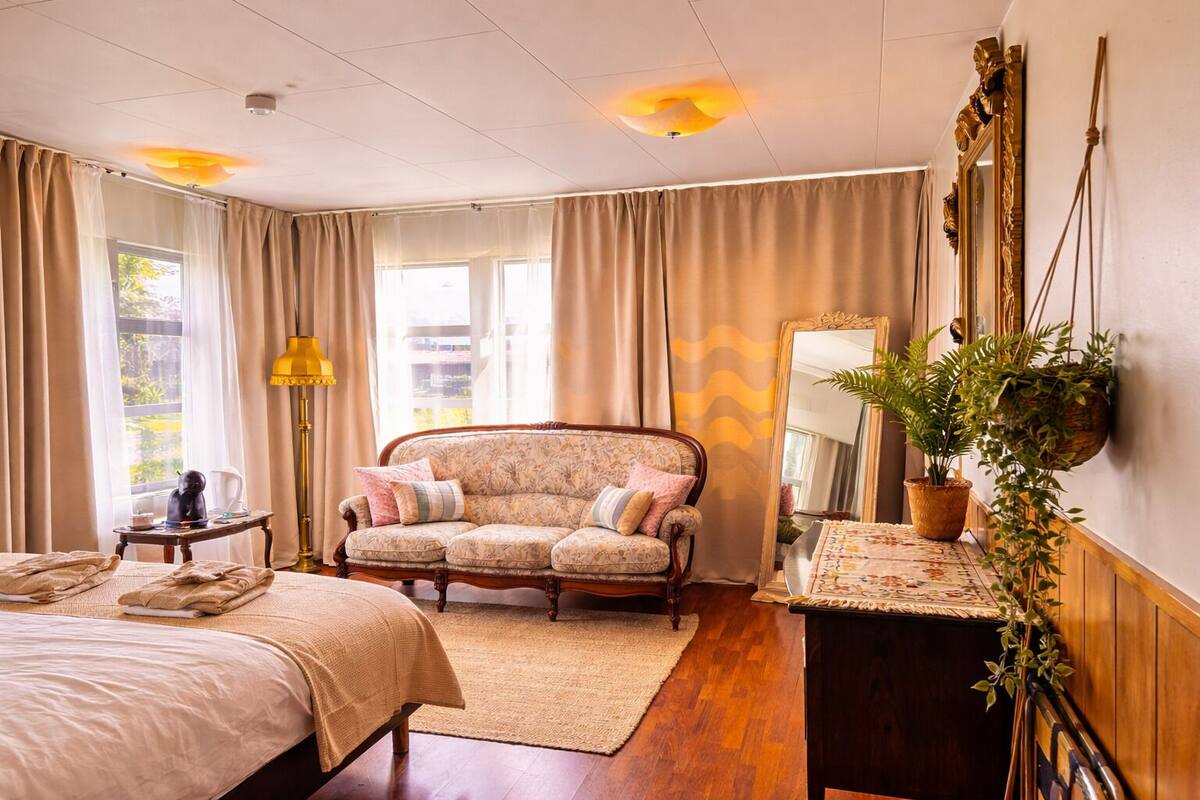 Une chambre à coucher avec un lit, un canapé, un bureau, un miroir et une plante en pot.