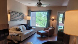 A modern living room with a sofa, armchair, and ottoman, a fireplace, and a large window with curtains. - Perfect 2nd floor condo with mtn & golf  views! Charm galore awaits you! (Tucson)