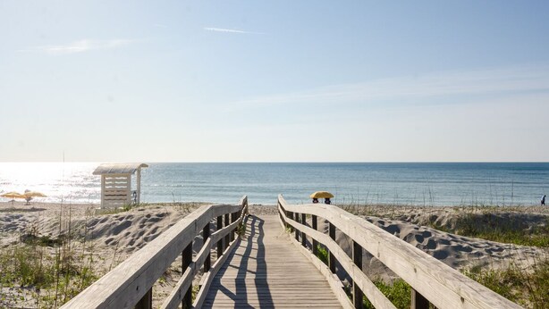 A wooden boardwalk leading to a beach with a lifeguard tower and a beach umbrella. - Brand New Construction short walk to the beach! (Carolina Beach)