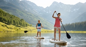 Deux personnes pratiquent le paddle sur un lac paisible, entouré de montagnes.