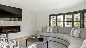 Ein modernes Wohnzimmer mit einem gebogenen grauen Sofa, einem runden Couchtisch und einem Kamin.