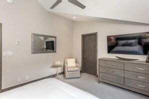 Een slaapkamer met een bed, een stoel, een dressoir, een televisietoestel en een deur.