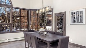 Ein moderner Essraum mit einem großen Tisch und Stühlen, große Fenster mit Blick auf Bäume und Schnee.