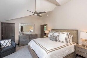 Une chambre à coucher comprenant un lit, une commode, une chaise, un ventilateur de plafond et une table de chevet.