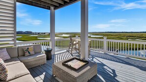 A covered outdoor deck with a wicker sofa and ottoman, a table with a tray, and a view of a marshland. - Dockside Hideaway: Enjoy Privacy and Scenic Views (Wrightsville Beach)
