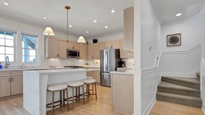 A modern kitchen with a central island, bar stools, stainless steel appliances, and pendant lighting. - Dockside Hideaway: Enjoy Privacy and Scenic Views (Wrightsville Beach)