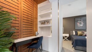 Una habitación moderna con un muro de listones de madera, un escritorio con una silla, una cama con colcha azul y un estante blanco con objetos decorativos.