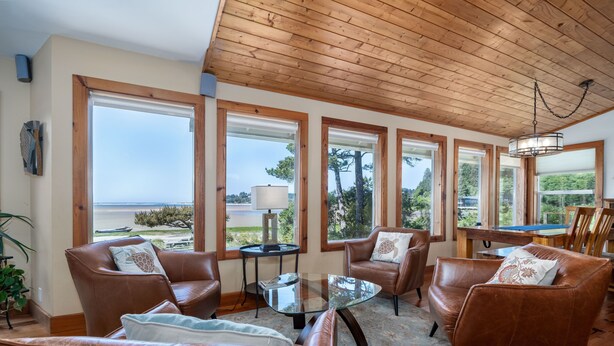 Un salon spacieux, doté de canapés en cuir, d’une table basse en verre et de grandes fenêtres offrant une vue sur la mer.