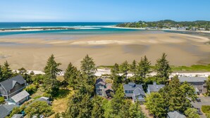 Vue aérienne d’une zone résidentielle côtière, avec des maisons entourées d’une végétation dense, une plage de sable et un océan bleu et limpide.