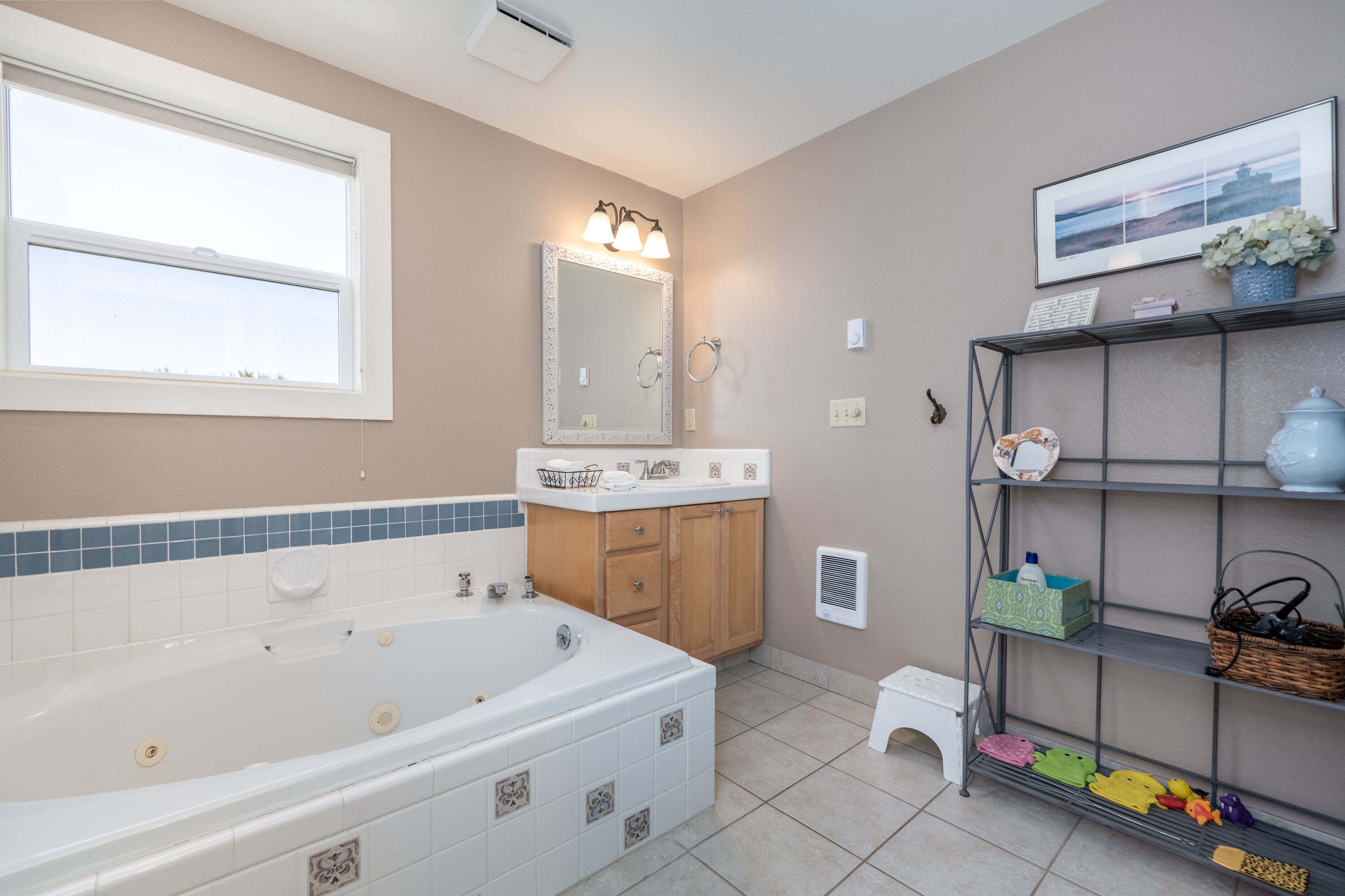 A bathroom with a large bathtub, a vanity with a mirror, and shelves with toiletries.