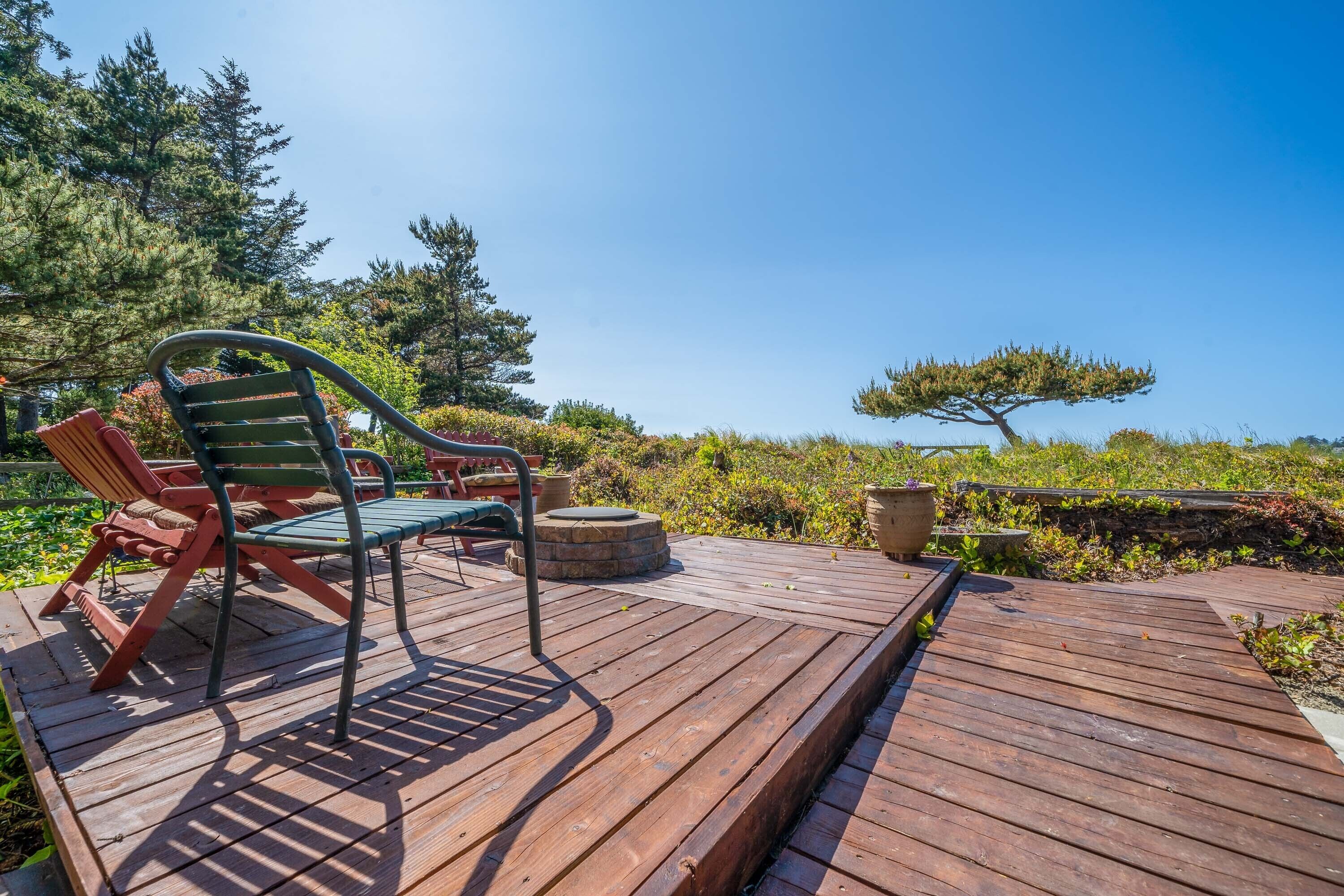 Een houten terras met buitenmeubilair, waaronder een groene stoel en een rode stoel, omringd door groen en een heldere lucht.
