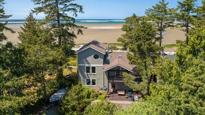 Une maison à deux étages avec un balcon, entourée d’arbres et offrant une vue sur la plage.