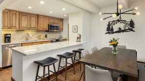 Une cuisine moderne avec des meubles en bois, un îlot central doté de tabourets de bar, une table à manger et un élément décoratif mural.