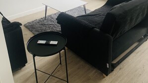 A modern living room with a flat-screen TV mounted on the wall, a black sofa, a small round coffee table, and a grey rug. - Impeccable 3 bed House in Brentwood (Brentwood)