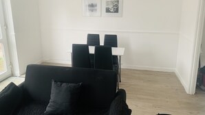 A room with a black sofa, a dining table with chairs, and two framed pictures on the wall. - Impeccable 3 bed House in Brentwood (Brentwood)